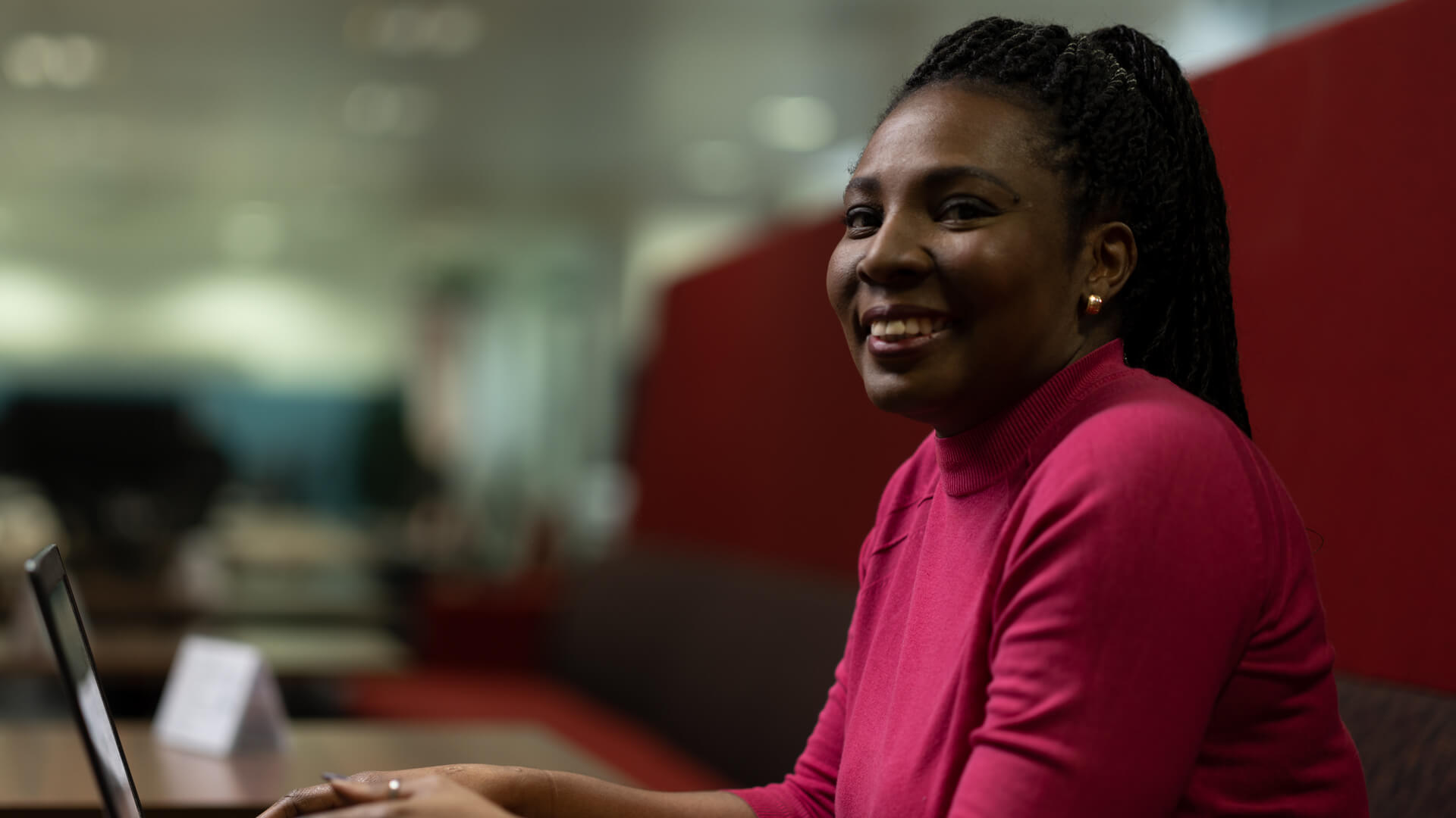 A female HMPO employee smiles to the camera whilst working on a laptop