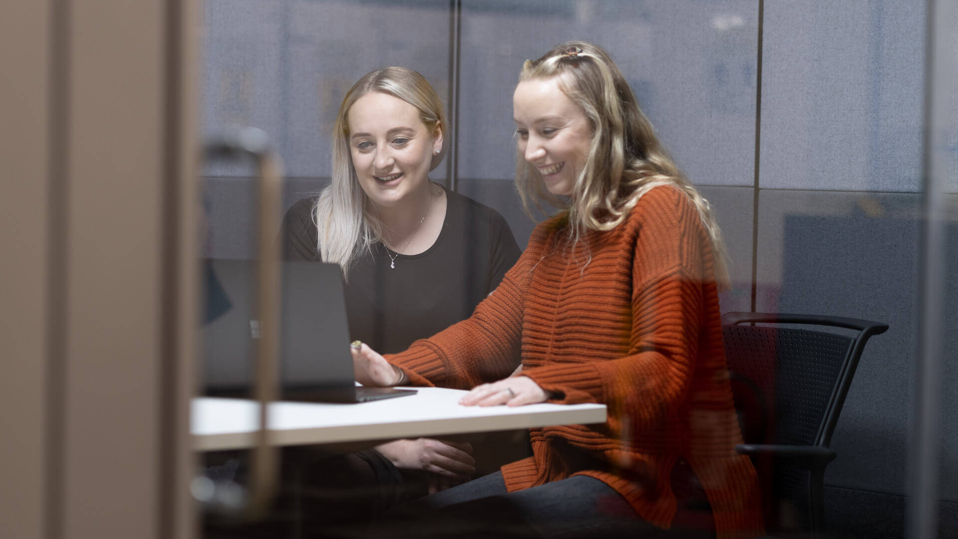 Two female Home Office employees smile as they work together on a laptop