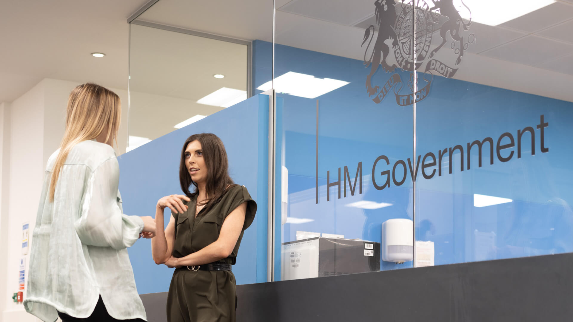 Two female HMPO employees talk in a modern office space.